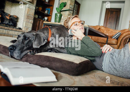 Woman talking on smart phone while lying on Great Dane at home Stock Photo