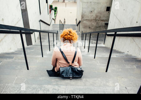 Rear view of woman with bag sitting on steps Stock Photo