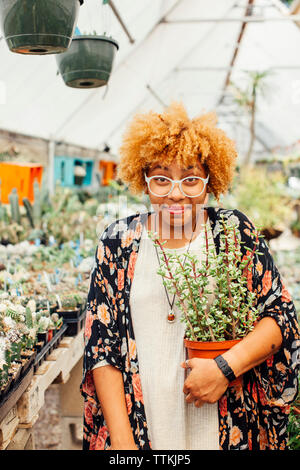 Portrait of woman holding potted plant while standing in nursery Stock Photo