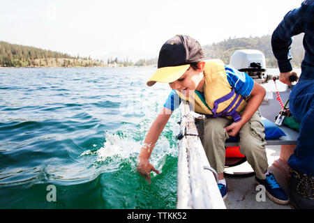 Happy son playing in water while traveling with father in motorboat on lake Stock Photo