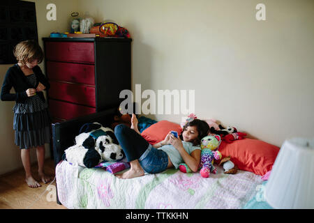 Girl getting dressed while sister using mobile phone on bed at home Stock Photo