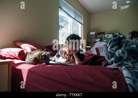 Girl looking at cat while lying on bed at home Stock Photo