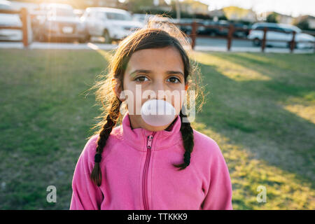 Portrait of girl blowing bubble gum while standing at park Stock Photo