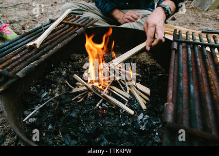 Cropped hand of man burning firewood in fire pit at campsite Stock Photo