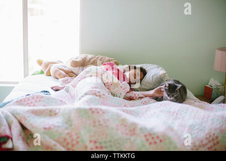 Girl petting cat while lying on bed Stock Photo