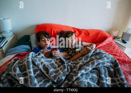 High angle view of siblings using smart phones while lying on bed Stock Photo