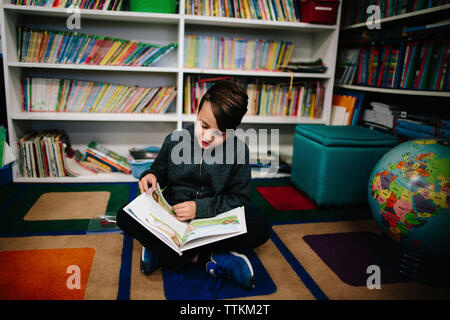 Boy studying while sitting against bookshelves in library Stock Photo