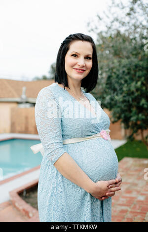 Pretty pregnant woman smiles for a portrait in front of swimming pool Stock Photo