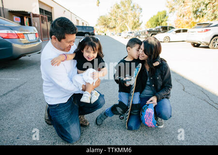 Family of four hug in a parking lot before skateboarding Stock Photo