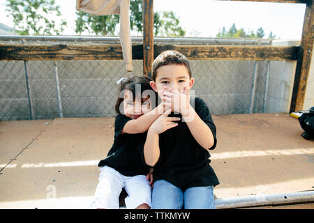 Siblings covering brothers mouth while sitting on half pipe Stock Photo