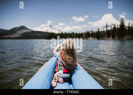 Rear view of girl sitting in inflatable raft on lake Stock Photo