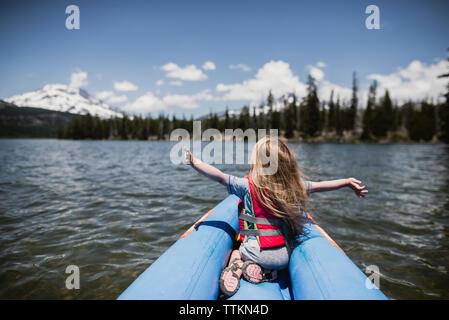 Rear view of carefree girl with arms outstretched sitting in inflatable raft on lake Stock Photo