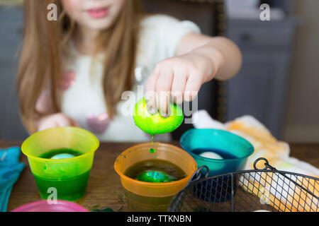 Midsection of girl dipping easter Egg in dyed water on table at home Stock Photo