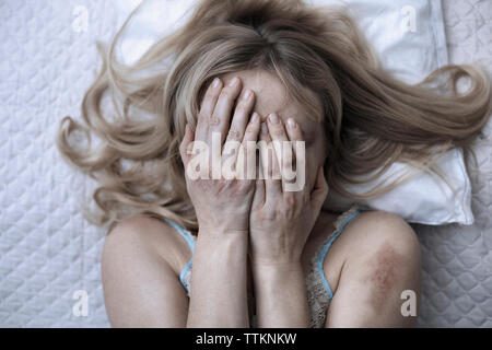Woman covering face with hands while lying on bed at home Stock Photo