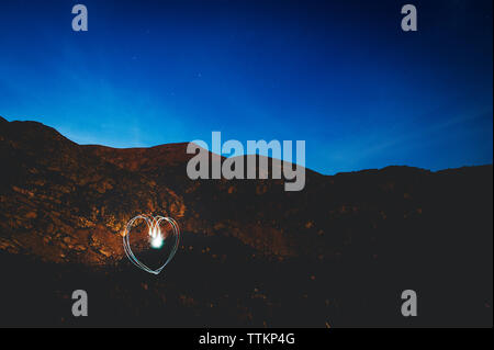 Heart shape light painting by mountain against blue sky at dusk Stock Photo