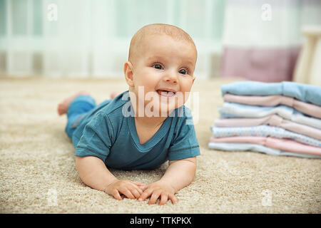 Smiling adorable baby with pile of clothes on the floor Stock Photo