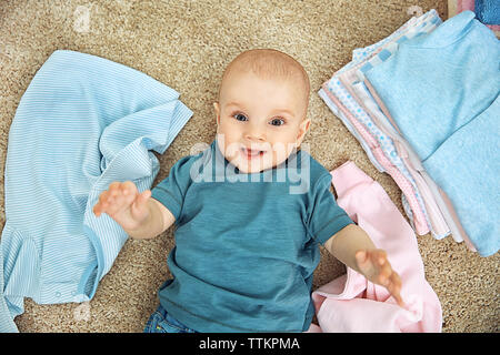 Smiling adorable baby with different clothes on the floor Stock Photo