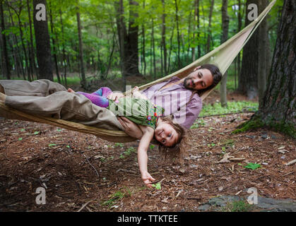 Happy father and daughter lying on hammock in forest Stock Photo