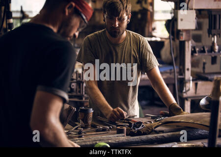 Blacksmith looking at coworker working at table in workshop Stock Photo