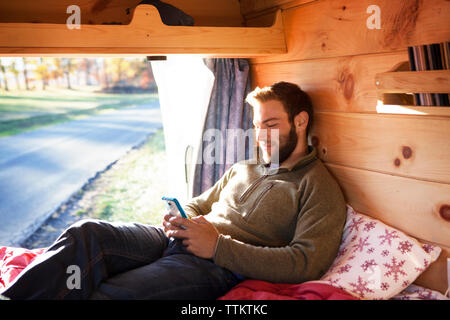 Man using smart phone while sitting on bed in camper van Stock Photo