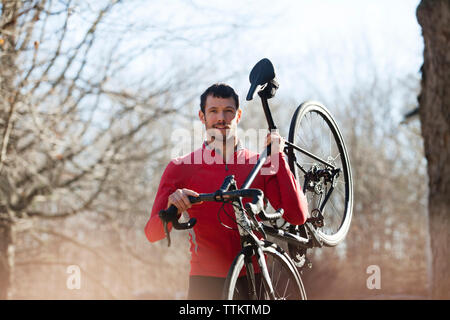 Portrait of athlete carrying bicycle in forest Stock Photo