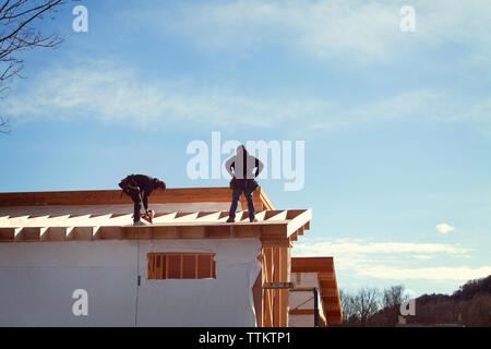 workers constructing house roof against sky during sunny day Stock Photo