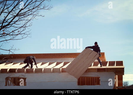 Low angle view of coworkers constructing house roof against sky Stock Photo