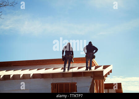 Low angle view of workers standing on roof beam against sky Stock Photo