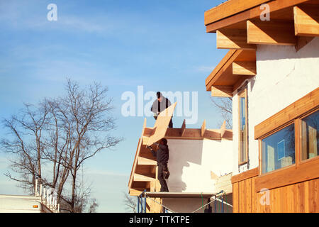 Low angle view of coworkers constructing house against blue sky Stock Photo
