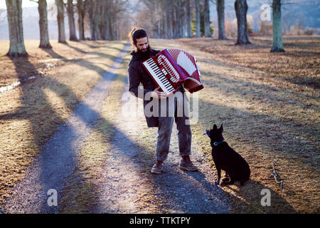 Full length of man playing accordion while dog sitting on field during vacation Stock Photo