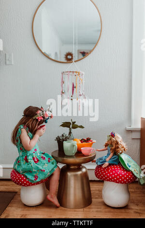 Little girl and doll having a tea party at home with flowers Stock Photo