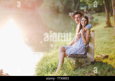 Portrait of couple sitting on bench by lake at park Stock Photo