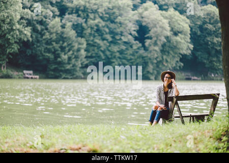 Portrait of woman sitting on bench at lakeshore in forest Stock Photo