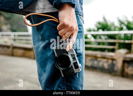Midsection of young man holding camera while standing on street Stock Photo