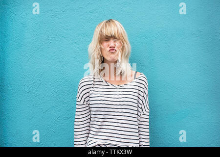 Young woman puckering lips while standing against blue wall Stock Photo