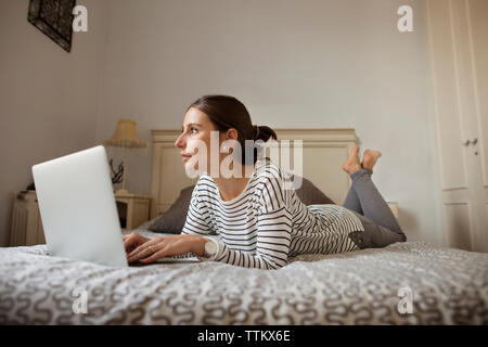 Thoughtful woman with laptop lying on bed at home Stock Photo