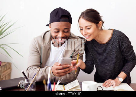 Happy male and female painters using smart phone at creative office Stock Photo