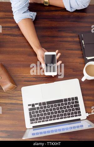 Directly above shot of businessman holding smart phone at desk in creative office Stock Photo