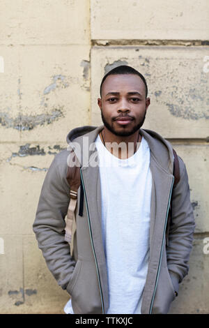 Portrait of confident young man standing with hands in pockets against wall Stock Photo