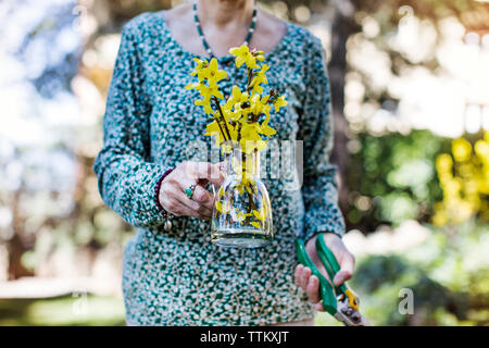 Midsection of senior woman holding flower vase and pliers at yard Stock Photo