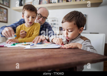 Senior man assisting grandsons in making drawings at home Stock Photo