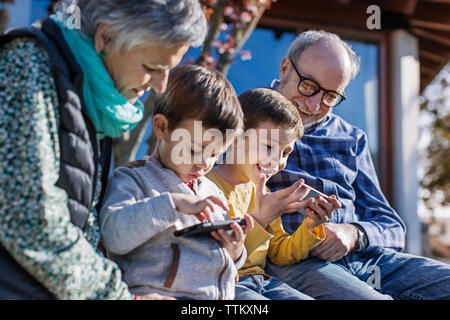 Happy grandparents and grandsons using smart phones in park Stock Photo