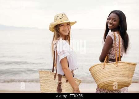 Side view portrait of happy female friends standing on shore at beach Stock Photo