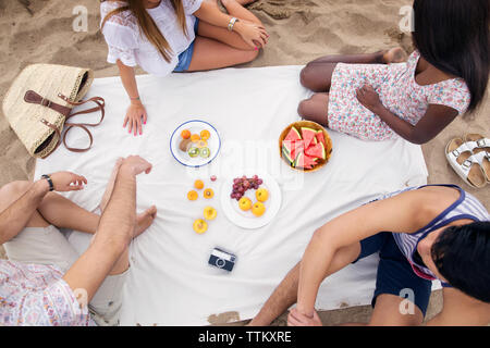 Overhead view of friends having fruits while sitting on beach Stock Photo