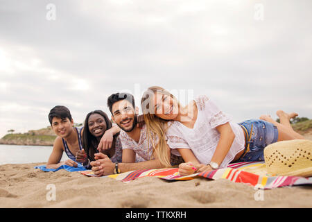 Portrait of cheerful friends lying on blanket at beach Stock Photo