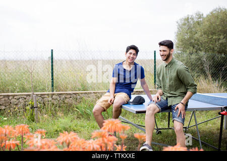 Happy male friends sitting on tennis table at yard Stock Photo