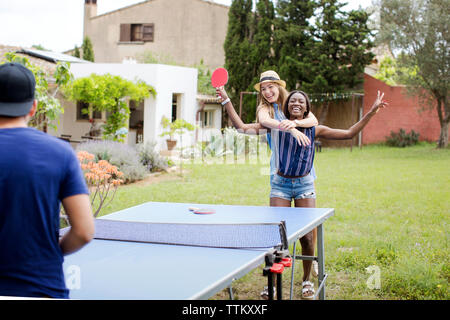 Cheerful women playing table tennis with male friend at yard Stock Photo