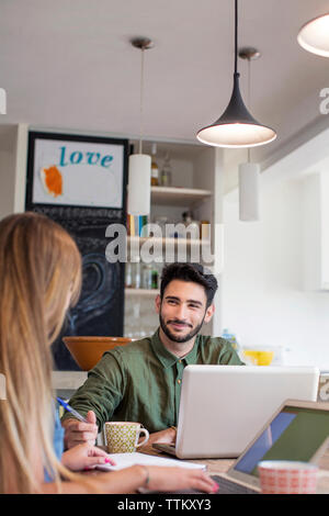 Smiling man looking at woman while using laptop at home Stock Photo