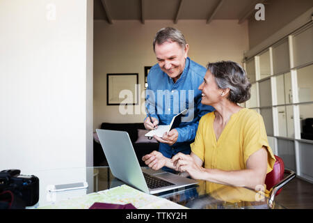 Senior man writing in diary while planning vacation with woman at home Stock Photo