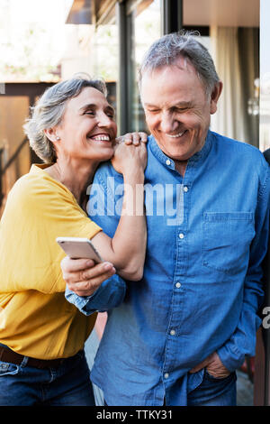 Cheerful woman looking at senior man using smart phone on porch Stock Photo